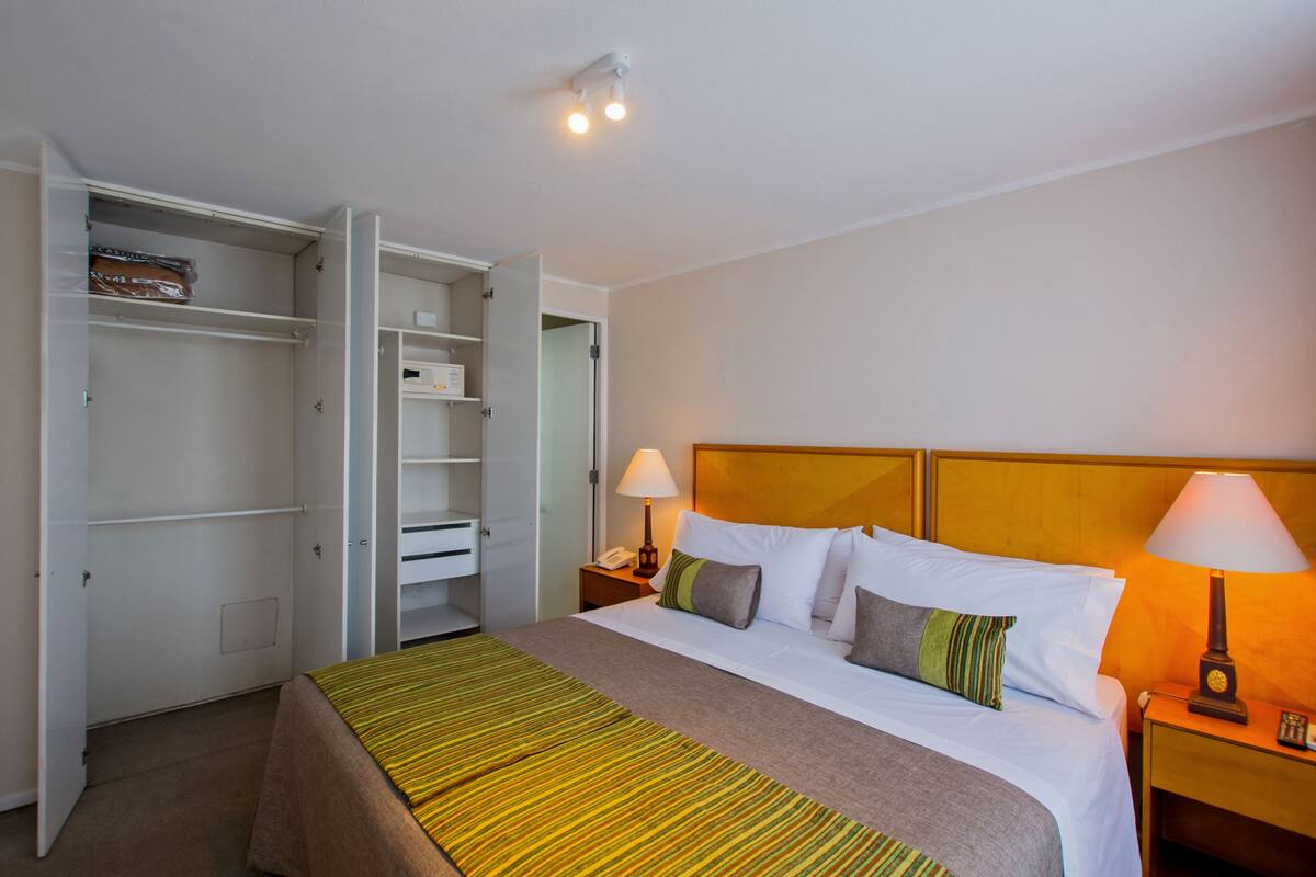 Ein Hotelzimmer mit Bett, Nachttisch mit Lampe, Kleiderschrank und Deckenleuchte.