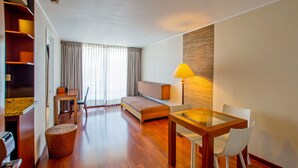 A modern hotel room with a wooden floor, a sofa, a dining table with chairs, a lamp, and a large window with curtains. - RQ Central (Santiago)
