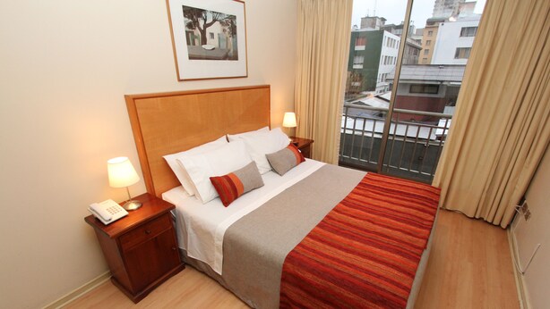 A hotel room with a bed, bedside lamps, a telephone, a window with curtains, and a framed picture on the wall. - RQ City Center (Santiago)