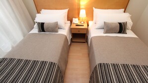 A hotel room with two beds, a nightstand with a lamp and phone, and a striped bedspread. - RQ City Center (Santiago)