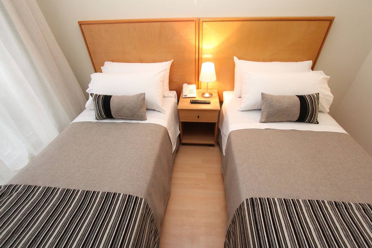 A hotel room with two beds, a nightstand with a lamp and phone, and a striped bedspread.