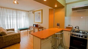 A compact living space with a kitchenette, a sofa, a dining table, and a painting on the wall. - RQ City Center (Santiago)