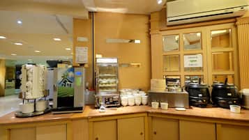 A coffee station with a coffee machine, a display of pastries, and a sign indicating the direction to the coffee area.