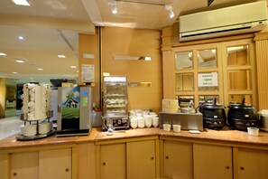A coffee station with a coffee machine, a display of pastries, and a sign indicating the direction to the coffee area.