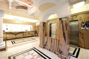 A lobby with marble flooring, an elevator, and a reception desk.
