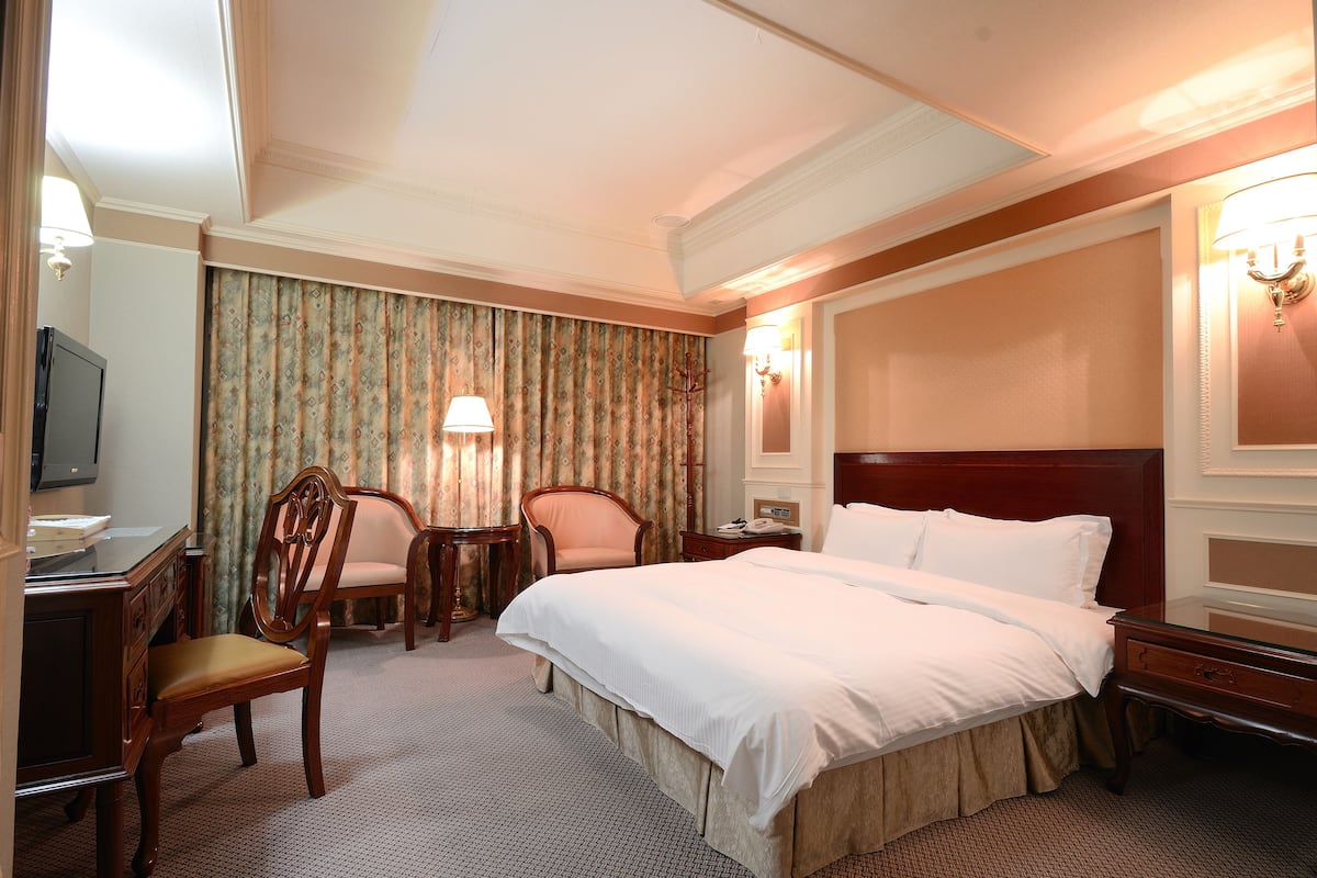 Une chambre d’hôtel avec un grand lit, un bureau avec une chaise, une télévision et une lampe.