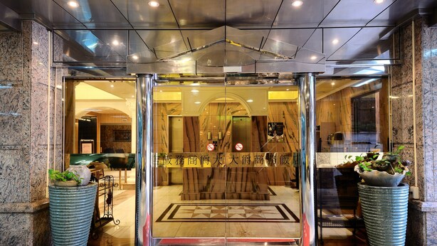 A hotel entrance with a glass door, a red carpet, and a large potted plant.