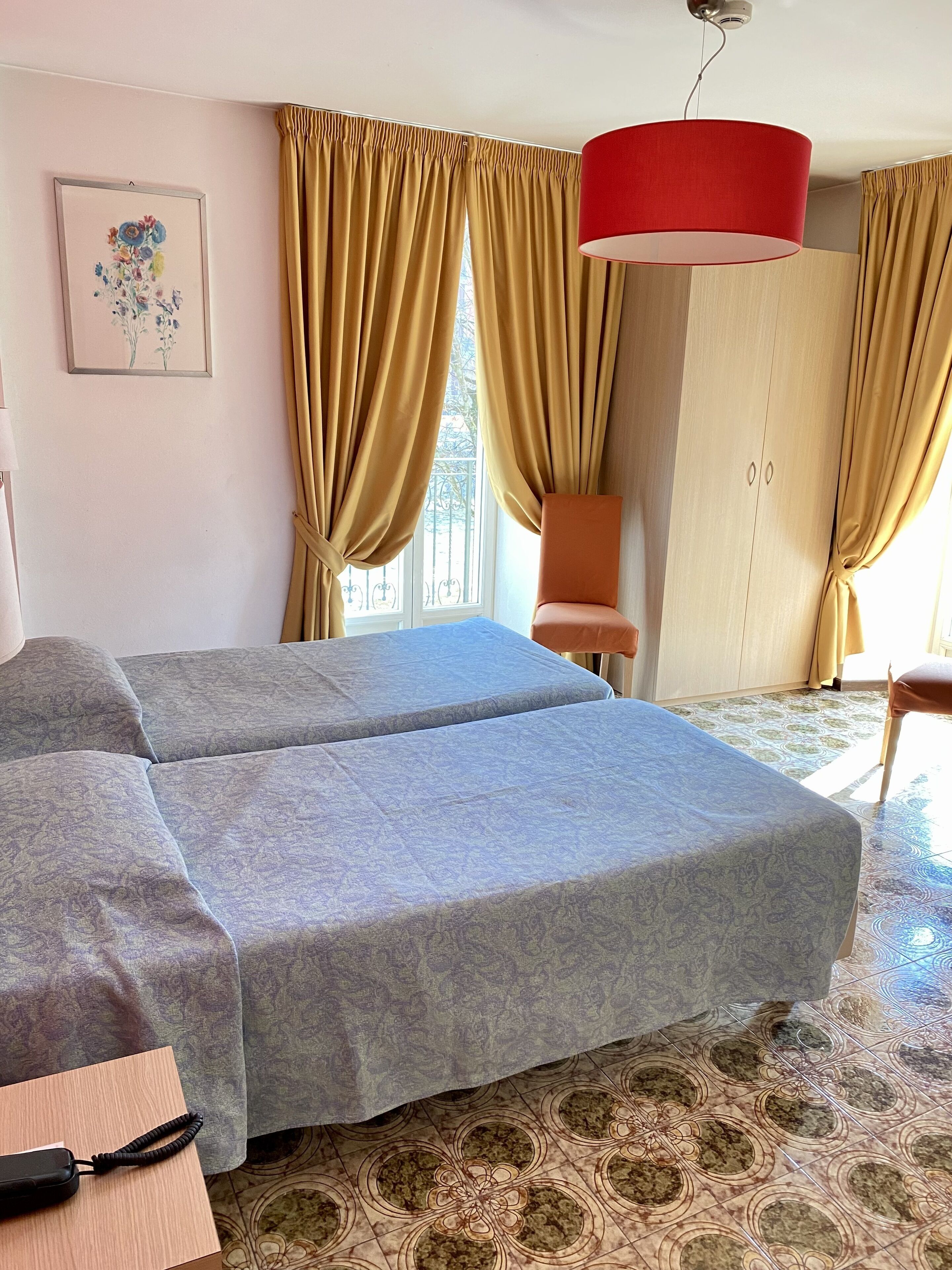 A hotel room with two beds, a wardrobe, a chair, and a red hanging lamp.