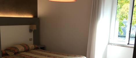 A bedroom with a bed, a red hanging lamp, a window with curtains, and a patterned rug.