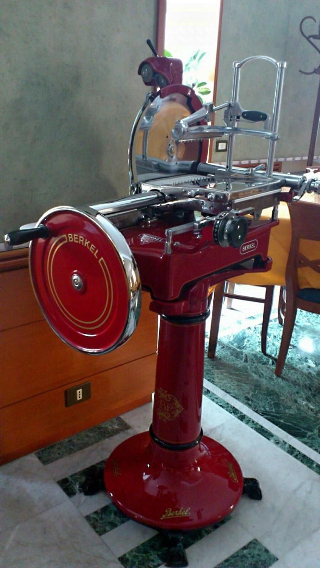 Une machine rouge d’époque, dotée d’un élément circulaire et d’une structure métallique sur le dessus, posée sur un sol carrelé.