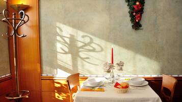 A dining area with a table set for two, featuring a white tablecloth, plates, glasses, and a basket of fruit.