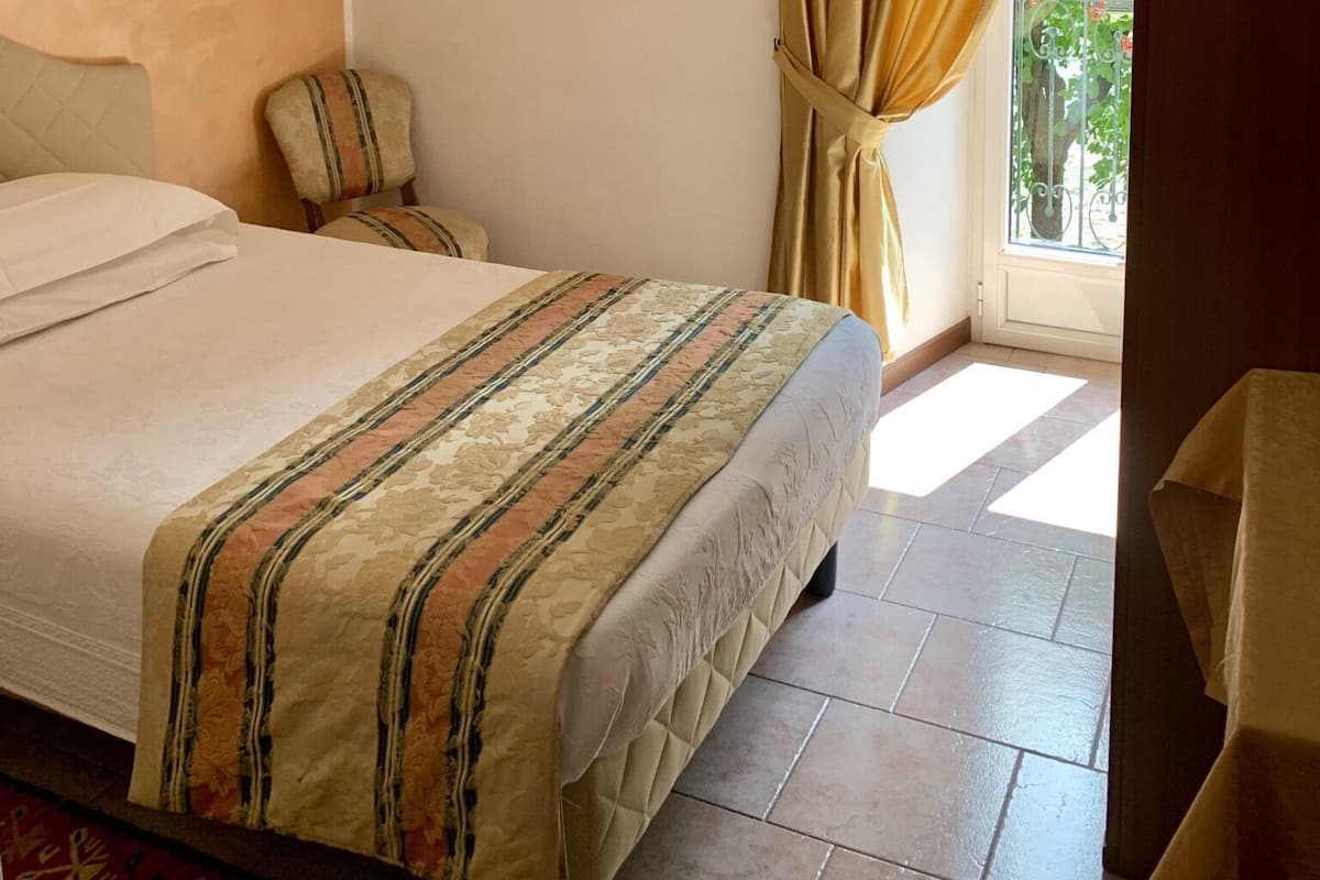 Ein Hotelzimmer mit Bett, Stuhl, einem Fenster mit Vorhängen und einer Deckenleuchte.