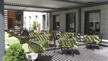 Un café en plein air avec des tables et des chaises, une petite fontaine et, en arrière-plan, la vue d’un bâtiment.