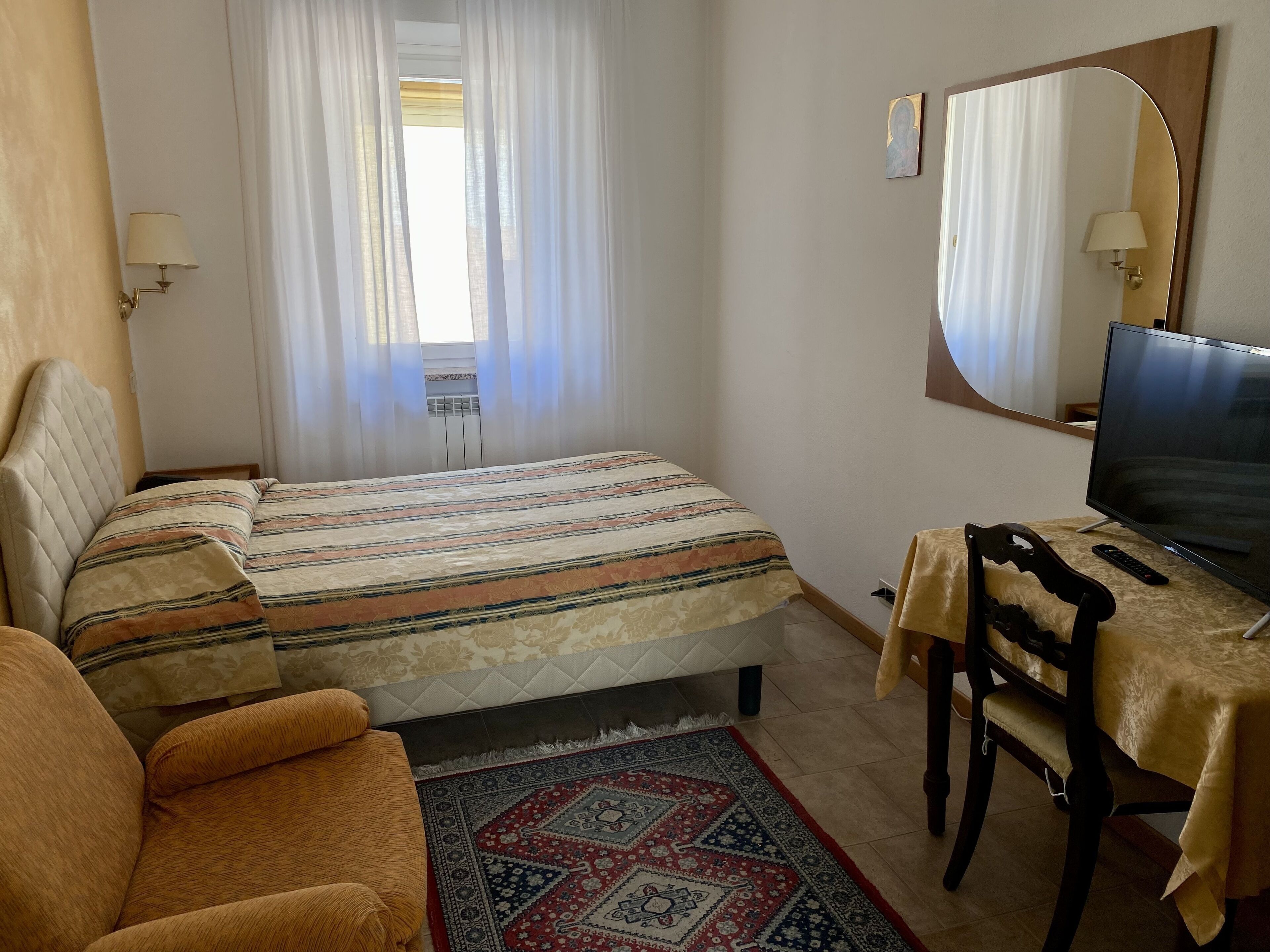 A bedroom with a bed, a desk with a chair, a television, and a window with curtains.