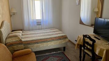 A bedroom with a bed, a desk with a chair, a television, and a window with curtains.