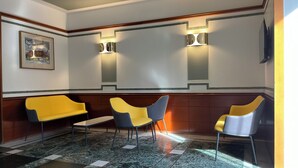 Un hall d’entrée avec un sol à carreaux, des chaises jaunes et grises, et une œuvre d’art encadrée accrochée au mur.