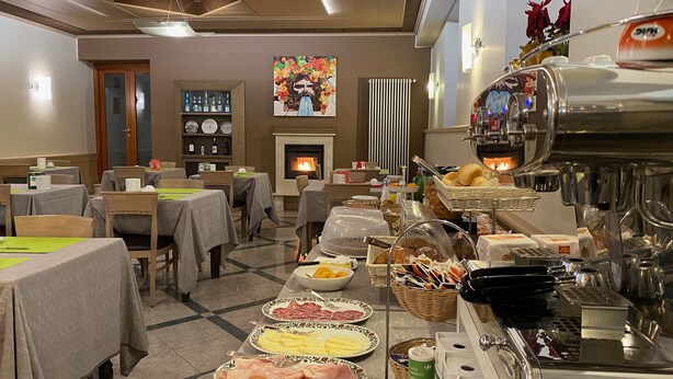 Une salle à manger d’hôtel avec des tables préparées pour le petit-déjeuner, une machine à café et une cheminée en arrière-plan.