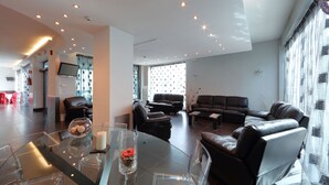 A spacious living area with leather sofas, a glass coffee table, and a flat-screen TV mounted on the wall. - Hotel Relax (Fiano Romano)