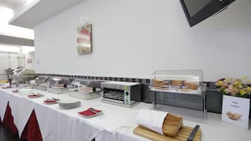 Disposição de buffet com diversos alimentos, um forno tostador e uma placa indicando uma estação de pães.
