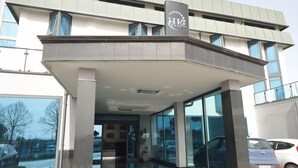 A modern building with a covered entrance, large windows, and a parking area. - Hotel Relax (Fiano Romano)