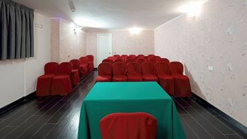 Un salón de conferencias con filas de sillas rojas, una mesa verde y una puerta blanca.