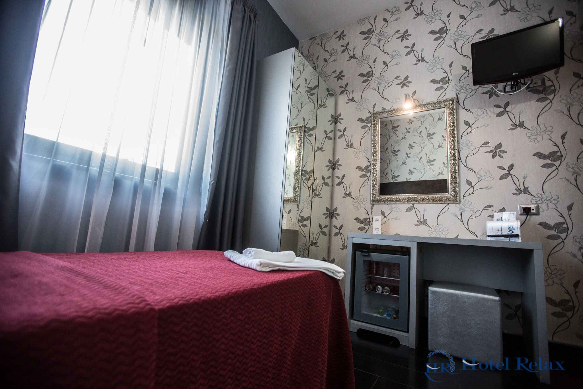 Una habitación de hotel con cama, tocador con espejo y televisión en la pared.