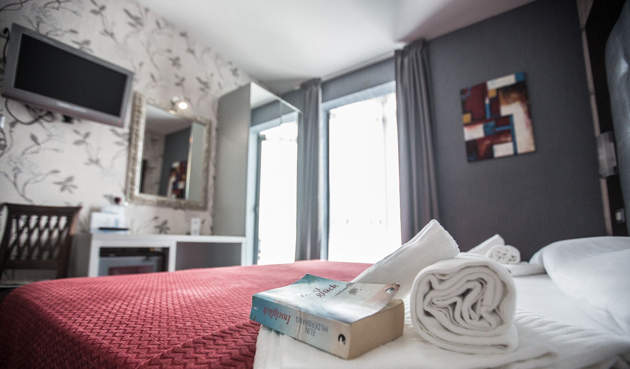 A hotel room with a bed, a desk, a chair, a TV, and a window.