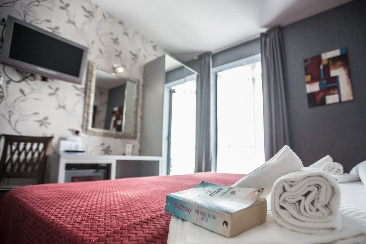 A hotel room with a bed, a desk, a chair, a TV, and a window.