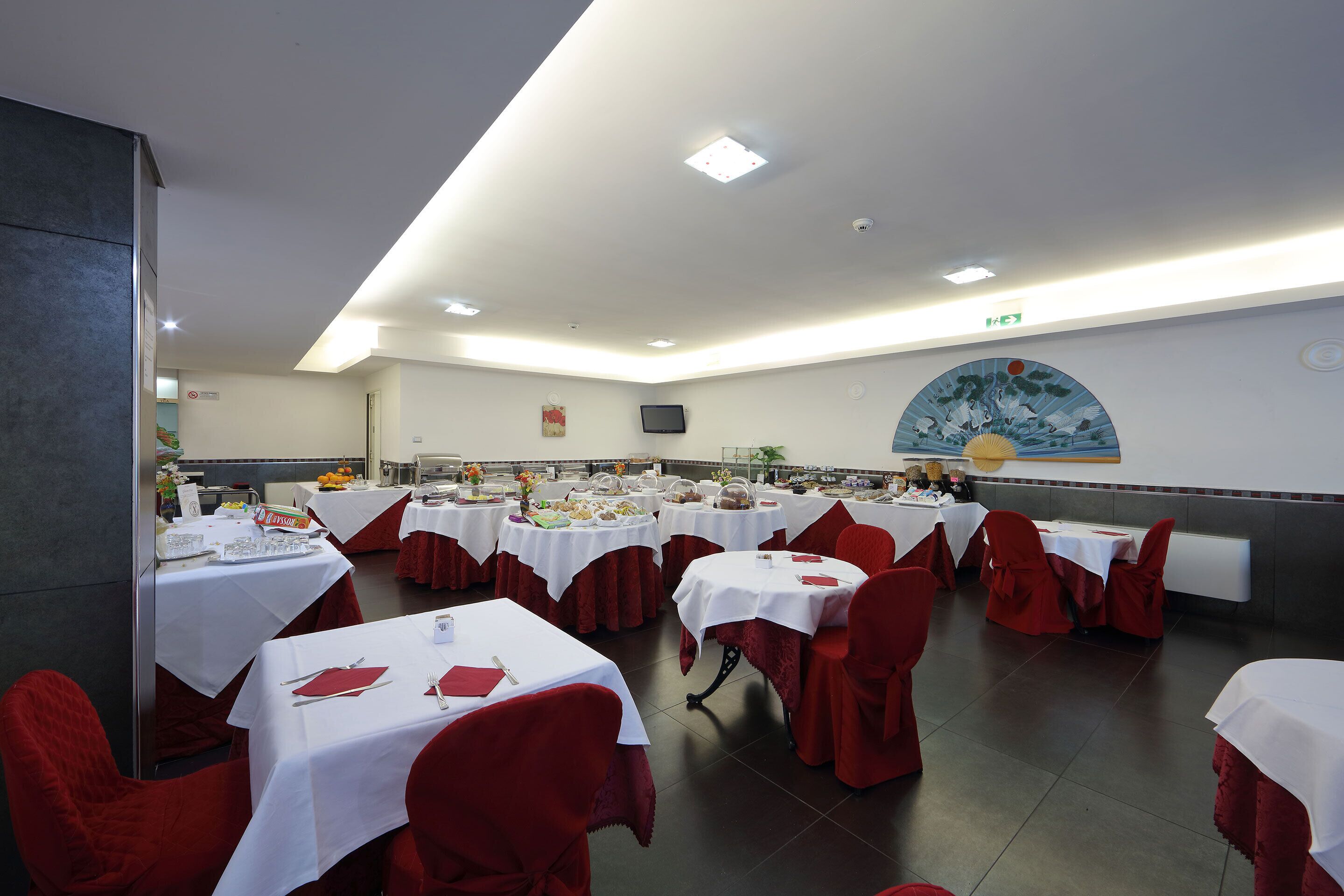 Un salón de banquetes con varias mesas redondas cubiertas con manteles blancos y sillas rojas.