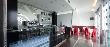 A modern restaurant with a long counter, glass partitions, and red-covered tables.
