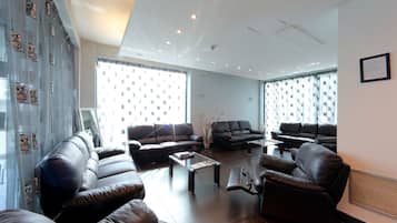 Ein geräumiges Wohnzimmer mit Ledersofas, einem Couchtisch und großen Fenstern mit gemusterten Vorhängen.