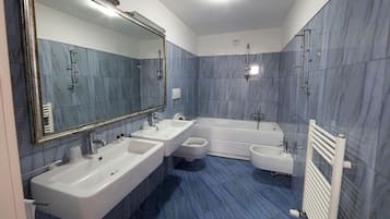 A modern bathroom with a large mirror, two sinks, a bathtub, and a toilet.