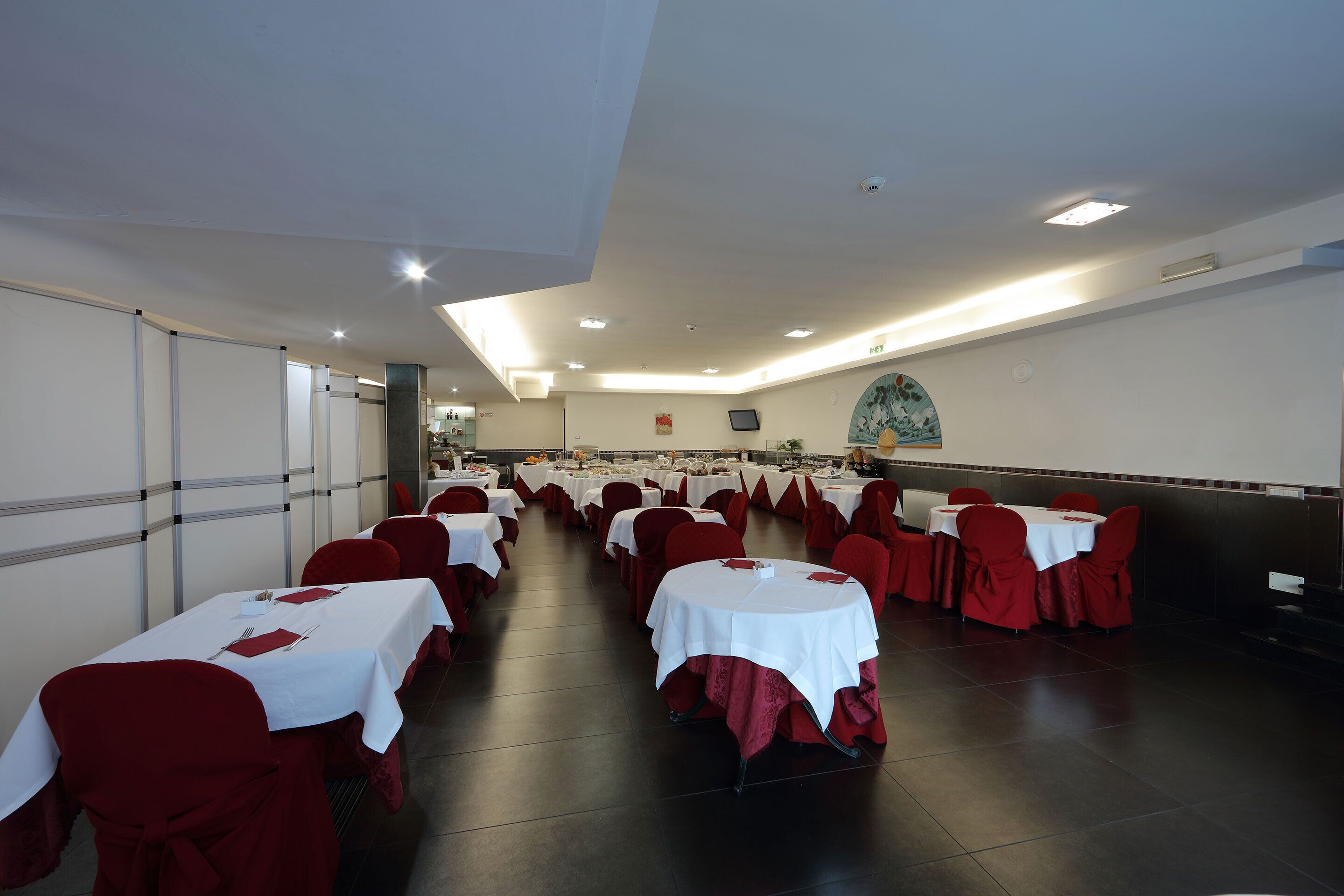 Un salón de banquetes con filas de mesas cubiertas con manteles blancos y sillas rojas.