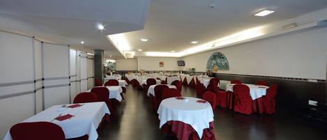 Un salón de banquetes con filas de mesas cubiertas con manteles blancos y sillas rojas.