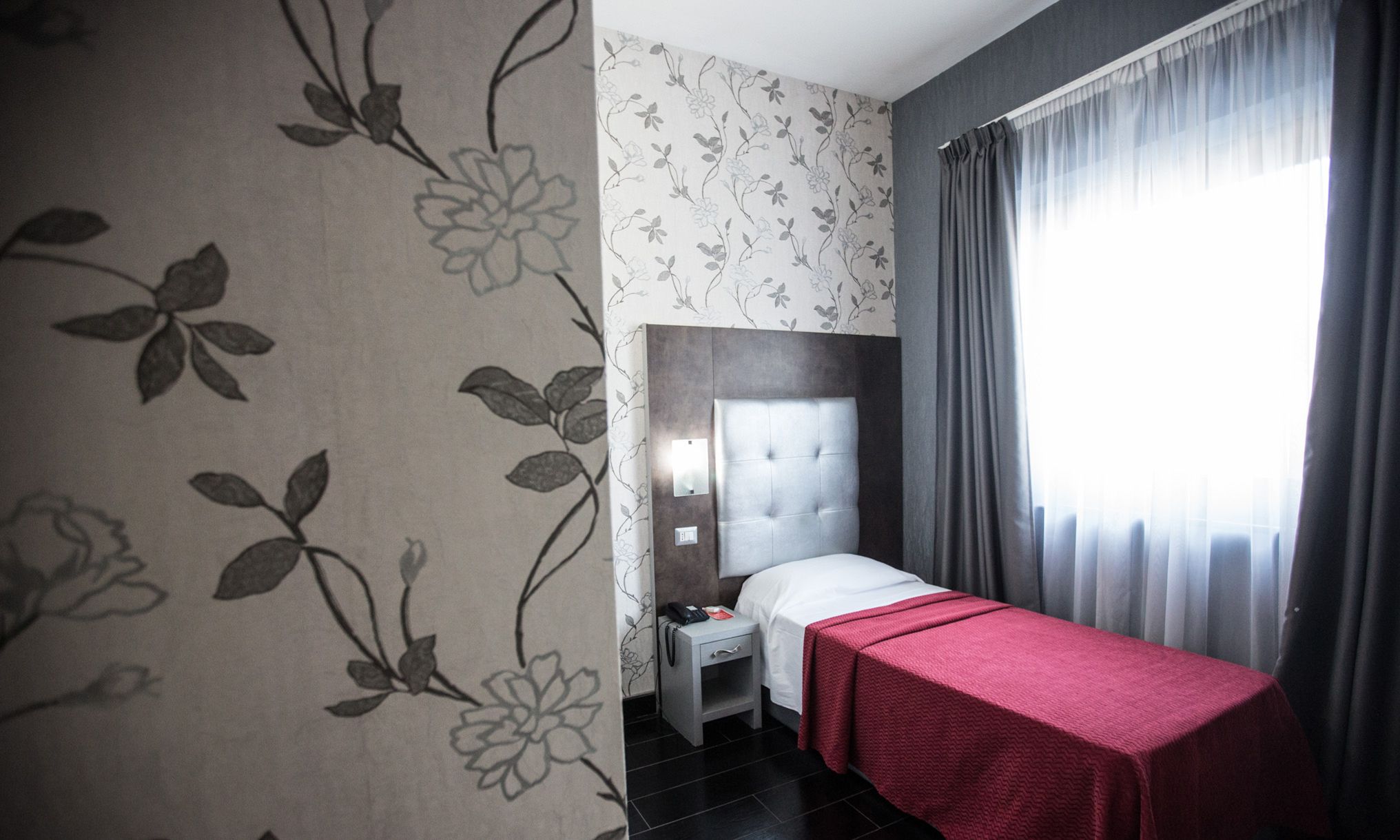 Una camera d'albergo con un letto, un comodino, un telefono e una coperta rossa.