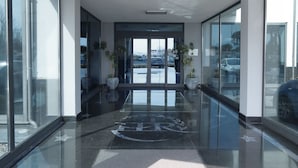 A modern lobby with glass walls, a polished floor, and a view of the parking area. - Hotel Relax (Fiano Romano)