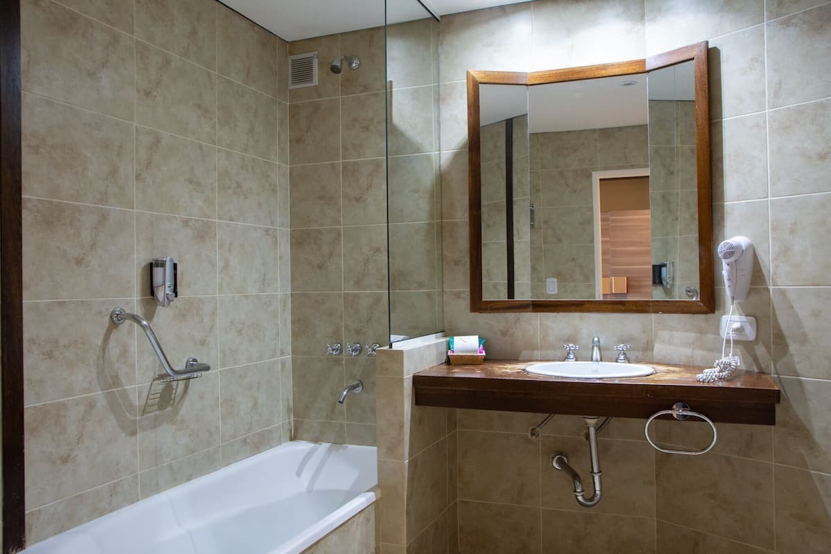 A bathroom with a bathtub, a sink, a mirror, and a hairdryer.
