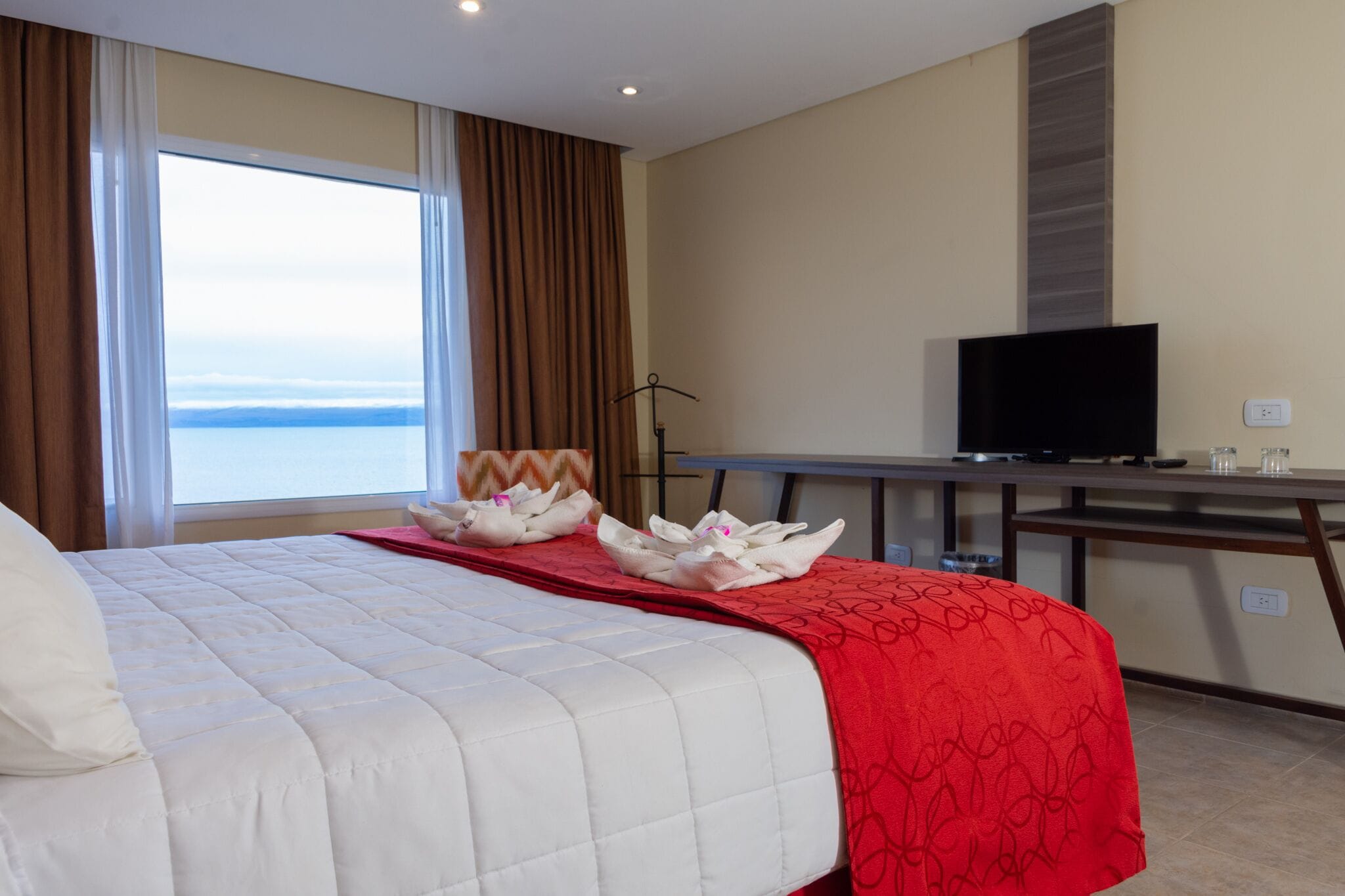 Een hotelkamer met een bed, een bureau, een televisie en uitzicht op zee.