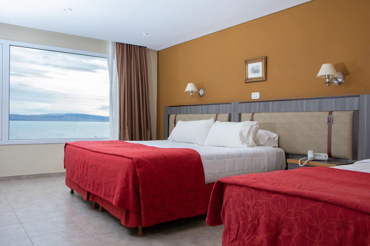 A hotel room with two beds, a large window with a view, and a telephone on the nightstand.