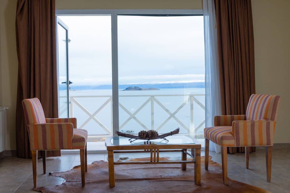 A room with two striped armchairs, a glass coffee table with a pinecone centerpiece, and a view of a body of water through a large window.