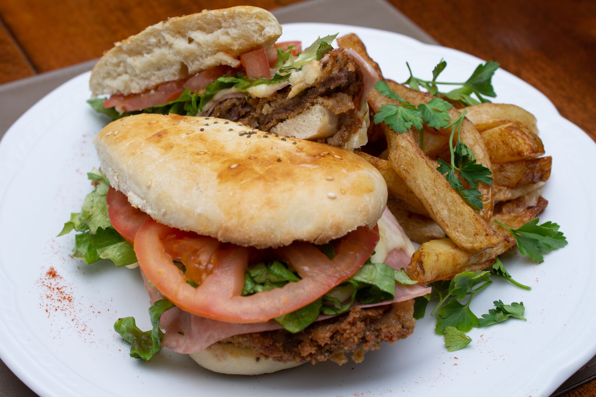 A sandwich with lettuce, tomato, and a fried item, served on a white plate.