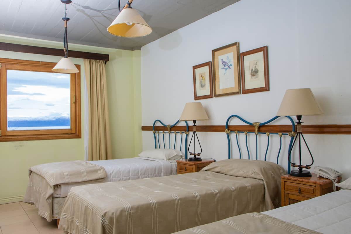 A hotel room with two beds, a wooden headboard, bedside lamps, a nightstand with a phone, and framed artwork on the wall.