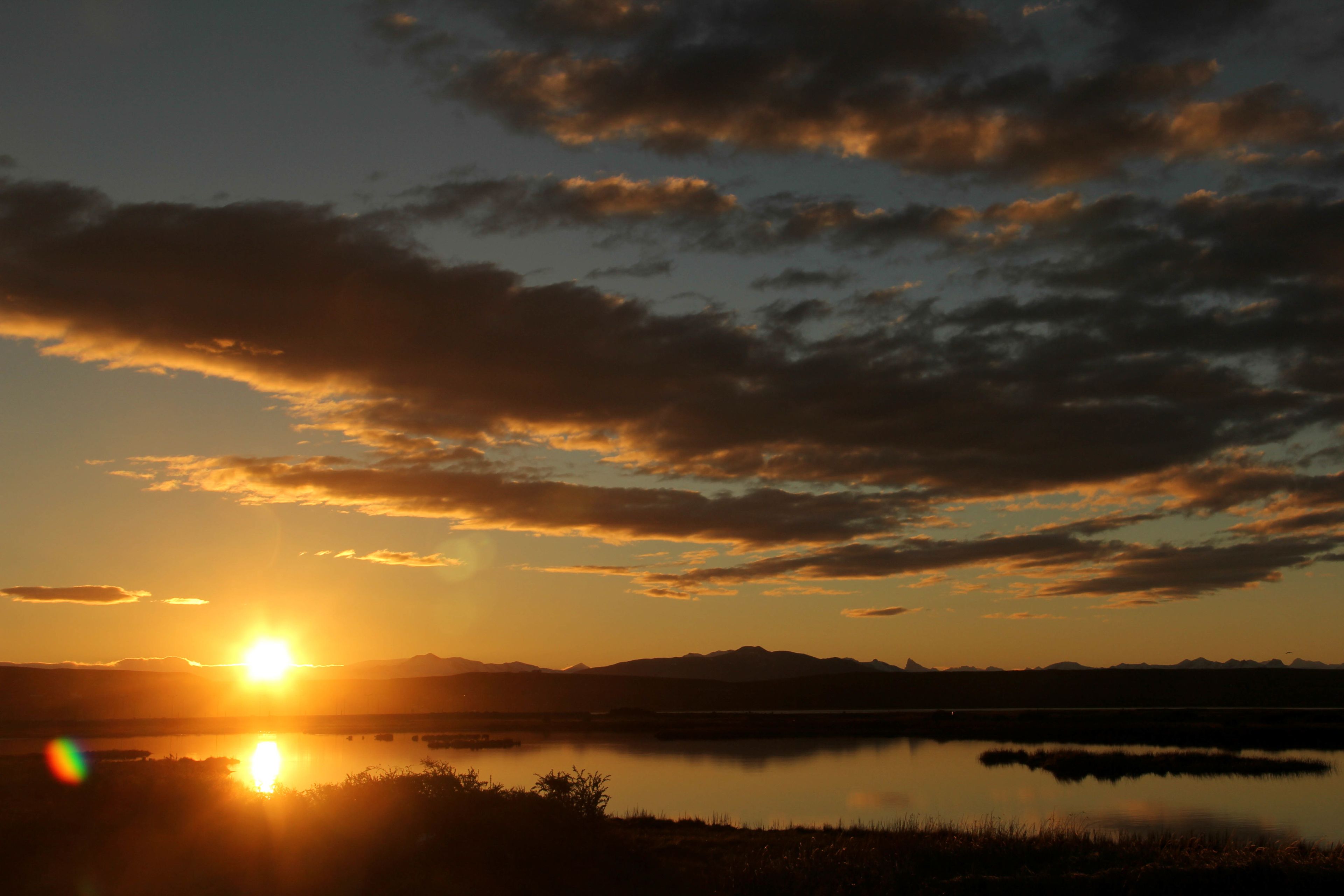Un coucher de soleil sur un lac paisible, avec des montagnes en arrière-plan.