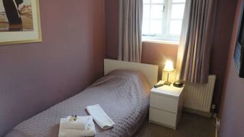 Una cama pequeña y ordenada con cabecera blanca, una mesita de noche con lámpara y un cuadro enmarcado en la pared.