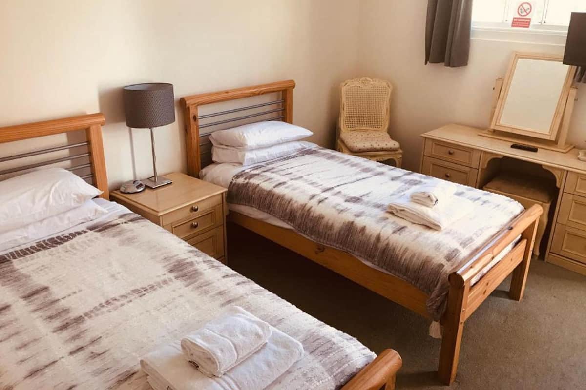 A hotel room with two single beds, a desk, a chair, a lamp, and a mirror.
