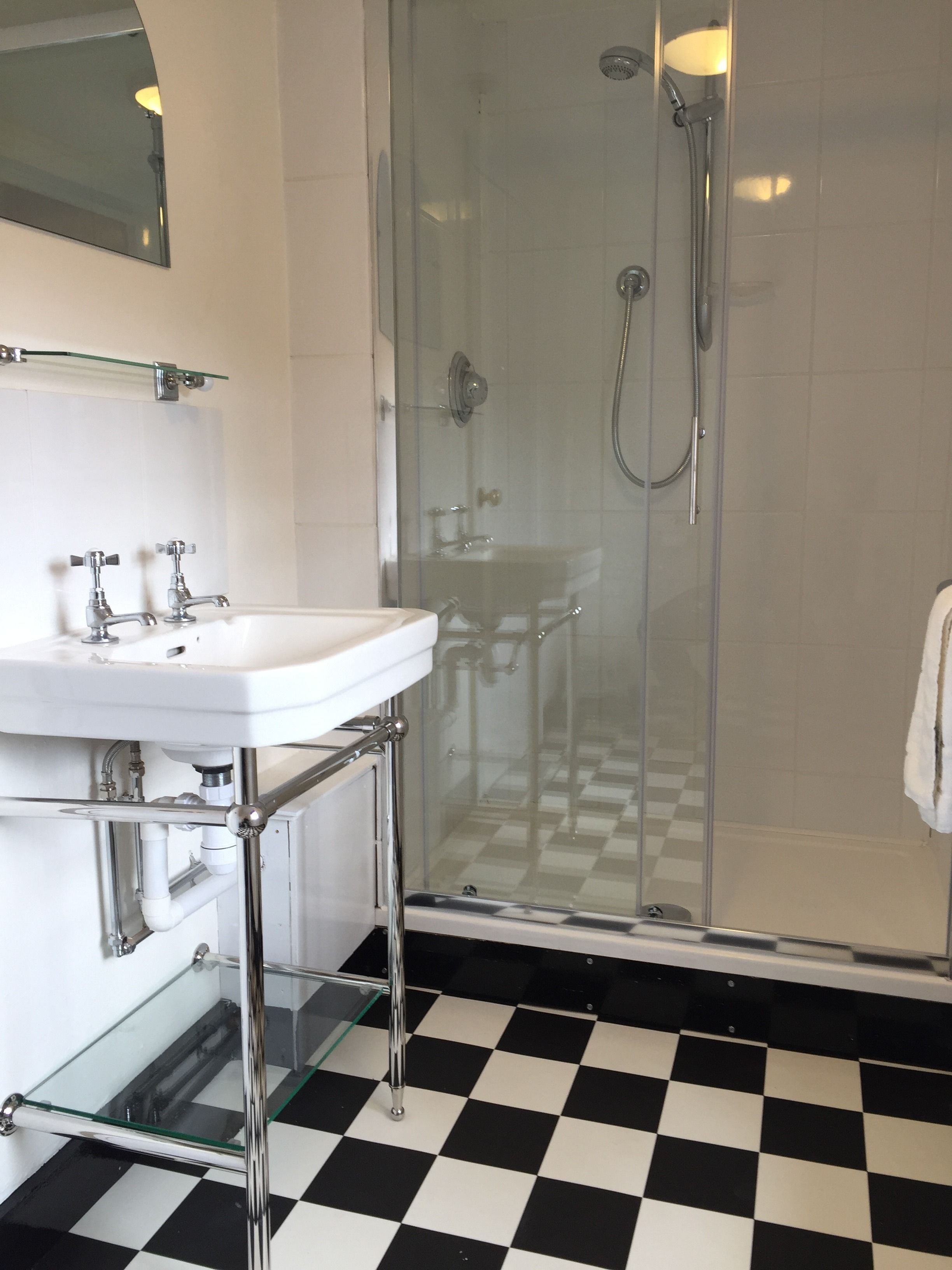 A bathroom with a glass-enclosed shower, a white sink, and a checkered floor.