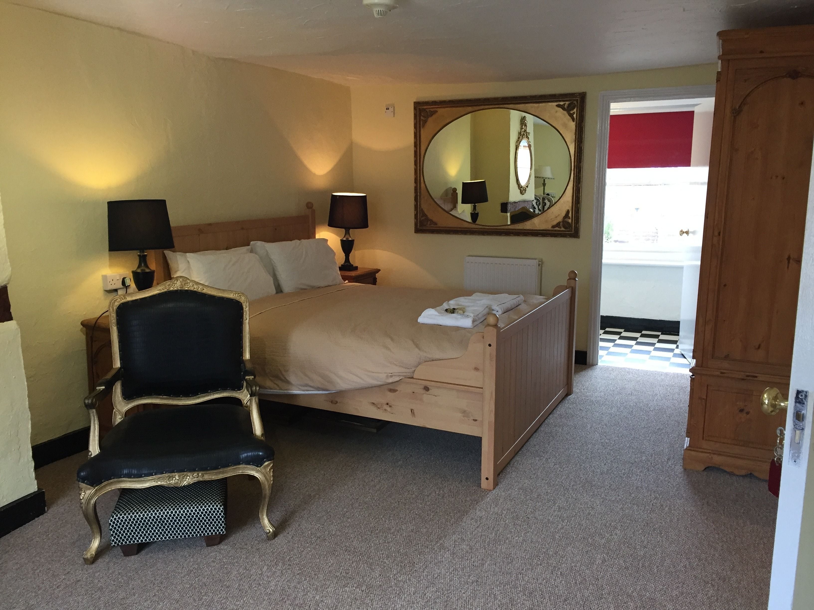 A bedroom with a wooden bed, two bedside lamps, a large mirror, a chair, and a wardrobe.