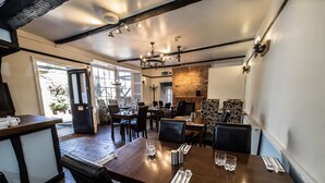 A restaurant with a brick wall, wooden tables, and black leather chairs. - Longs Inn (Milton Keynes)