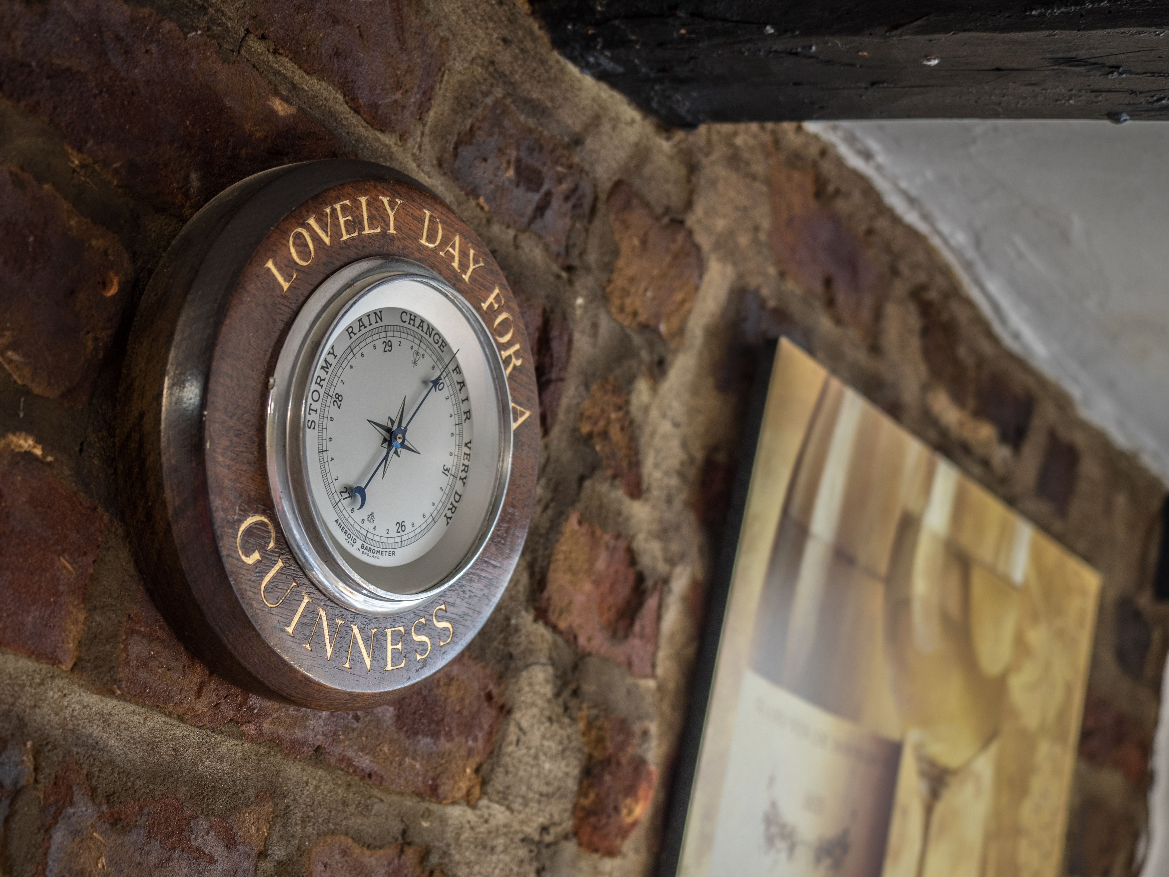 A barometer mounted on a brick wall with the text "STORMY RAIN CHANGE FAIR VERY DRA" and "GUINNESS" visible.
