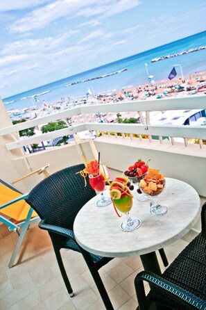 A balcony with a table set for two, overlooking a beach with boats and umbrellas.